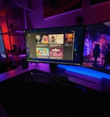 A gaming setup featuring multiple screens with vibrant game-related images illuminated by colorful LED lighting. The environment is dimly lit, highlighting the vivid displays on the monitors. A keyboard is visible on the desk beneath the central monitor.